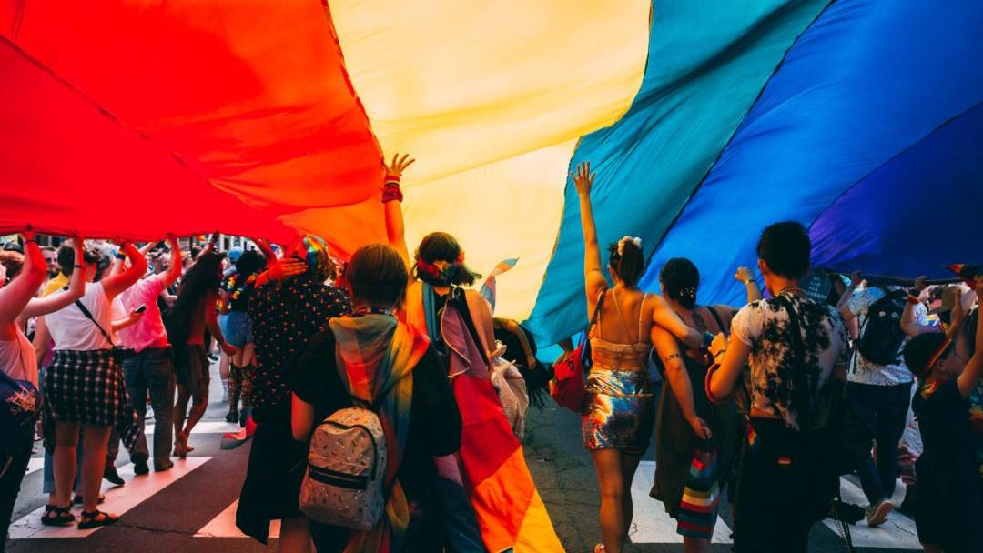 Eine Gruppe von Menschen demonstriert auf der Straße unter einer riesigen Regenbogenflagge