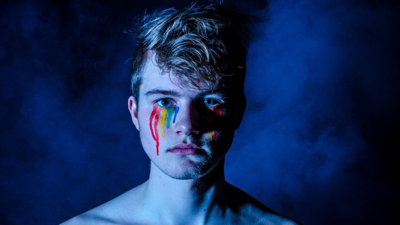 Eine Person mit einem geschminkten, verlaufenen Regenbogen im Gesicht